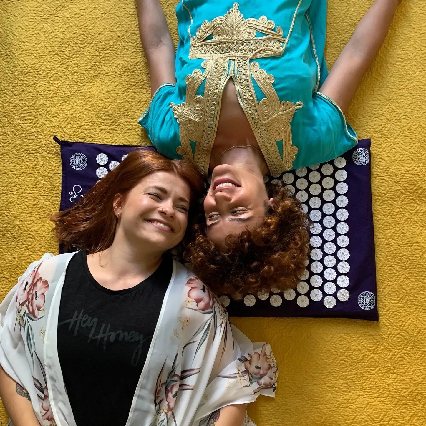 Two women are visibly happy lying head to head on a Shakti mat.